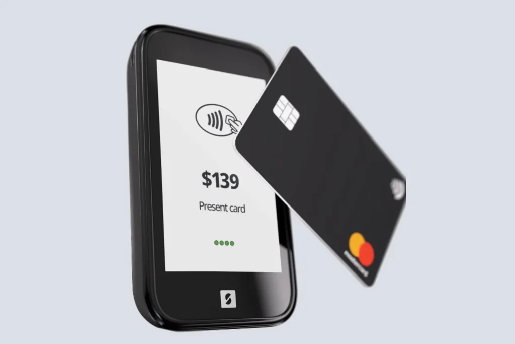 Black credit card tapping a payment terminal showing a contactless prompt