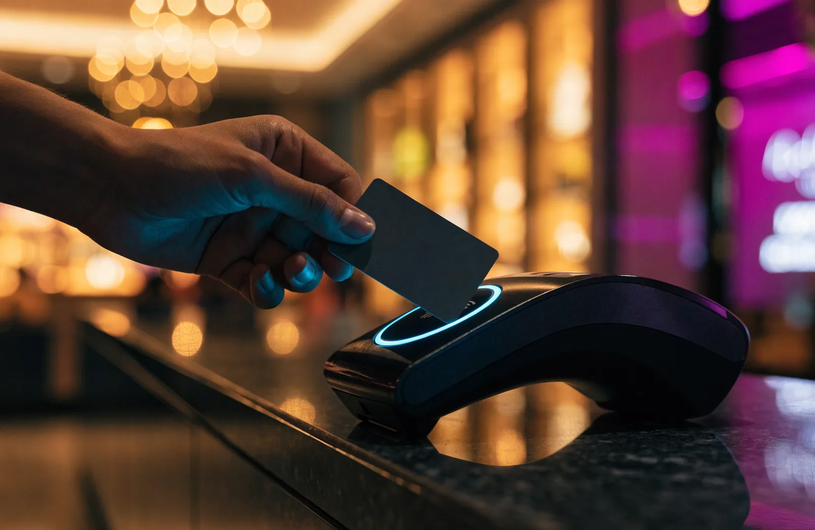 Hand tapping a card on a payment terminal with a glowing blue ring